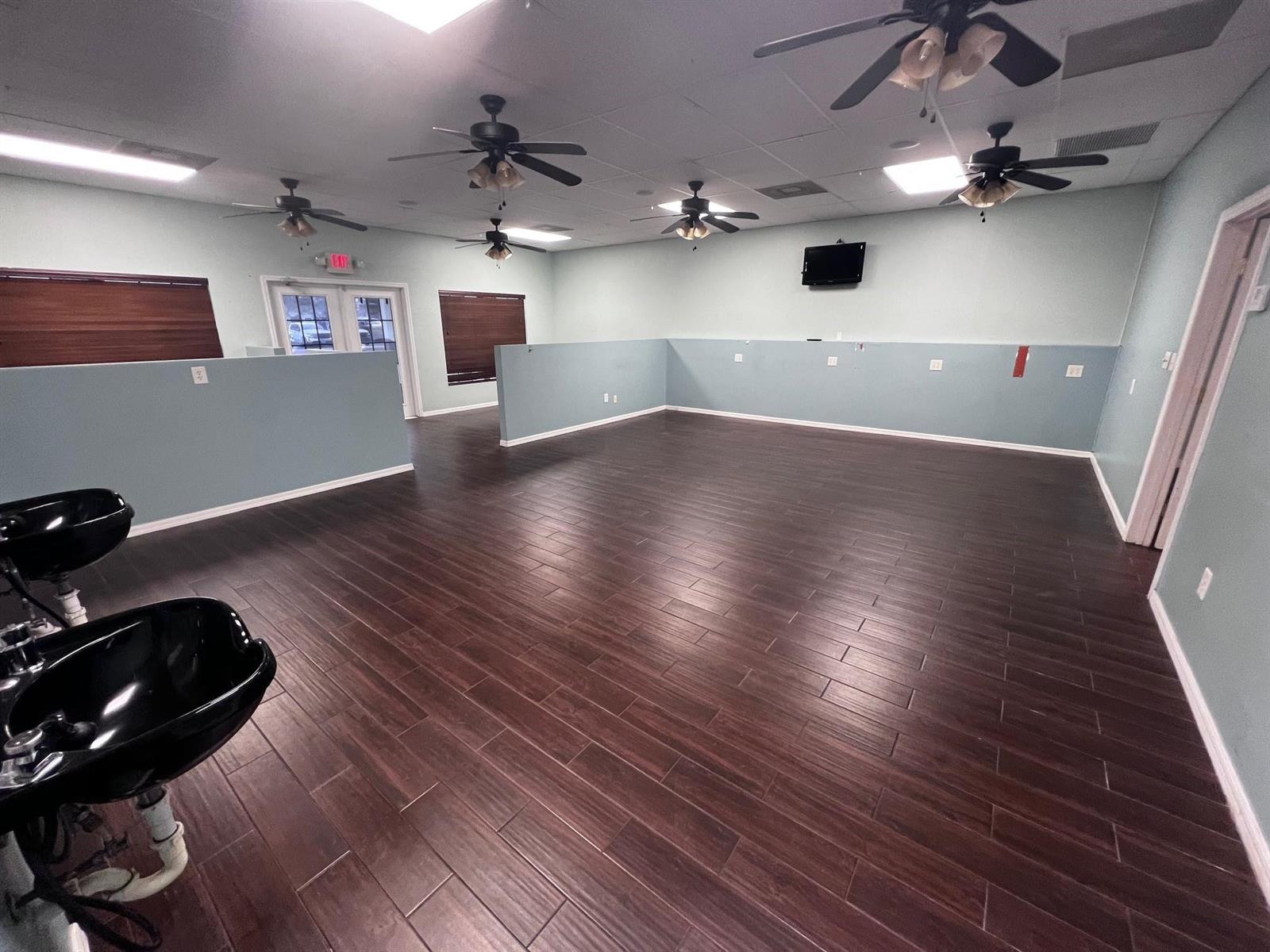 An empty salon space features dark wood-look flooring, light blue walls, and multiple ceiling fans — 3731 Oleander # 102, Fort Pierce FL 34982, FORT PIERCE, FL