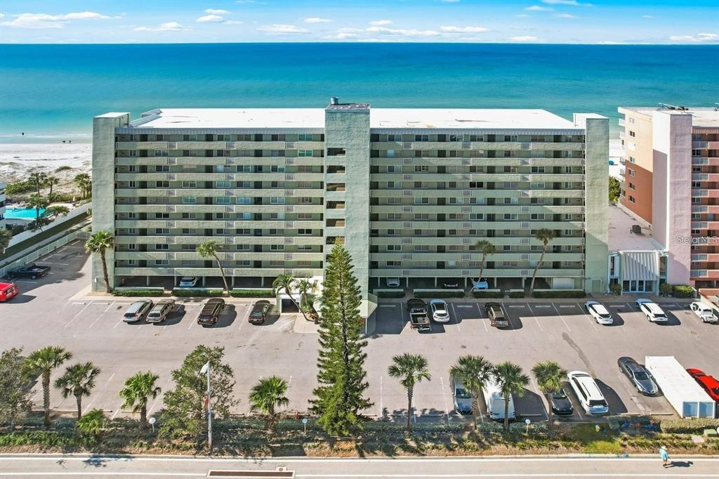 An aerial view of a multi-story beachfront apartment building with a parking lot in front — 20000 GULF BOULEVARD UNIT 707, INDIAN SHORES, FL