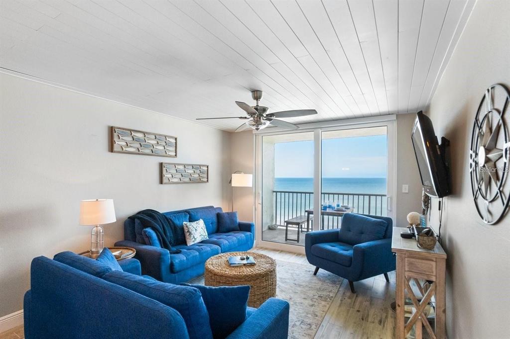 A living room with blue sofas, a round wicker coffee table, and a balcony view — 20000 GULF BOULEVARD UNIT 707, INDIAN SHORES, FL