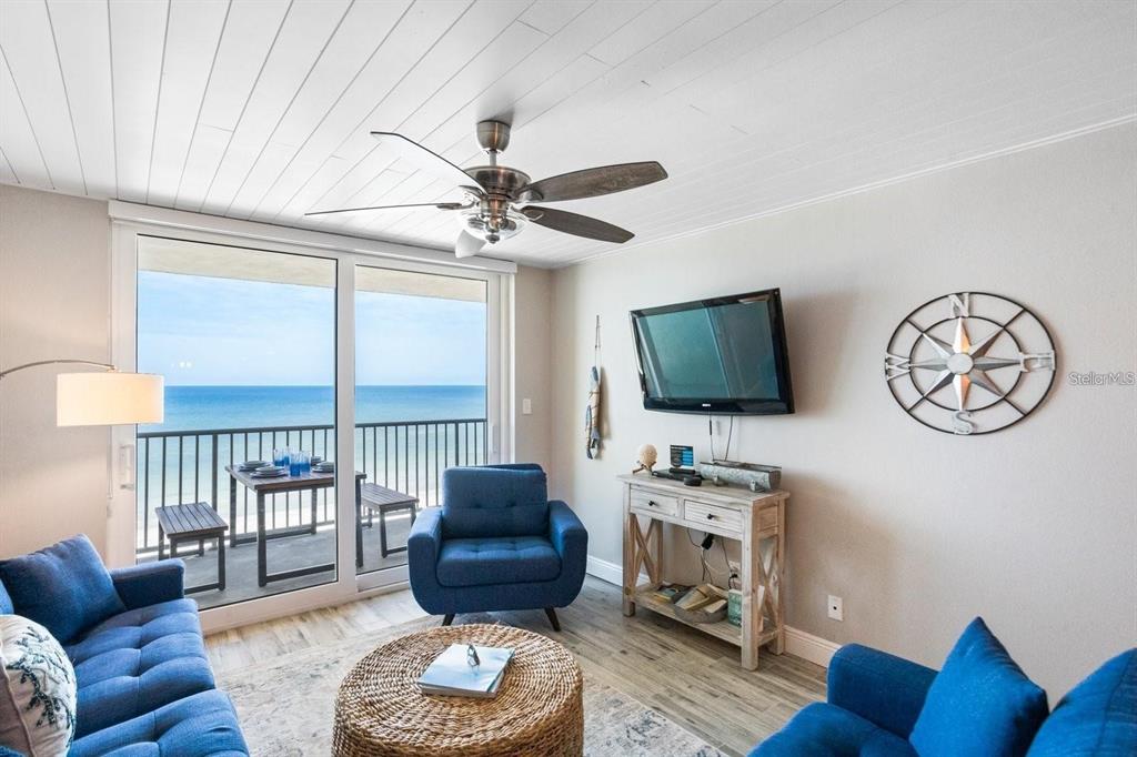 A living room features blue furniture, a round woven coffee table, and a balcony view — 20000 GULF BOULEVARD UNIT 707, INDIAN SHORES, FL