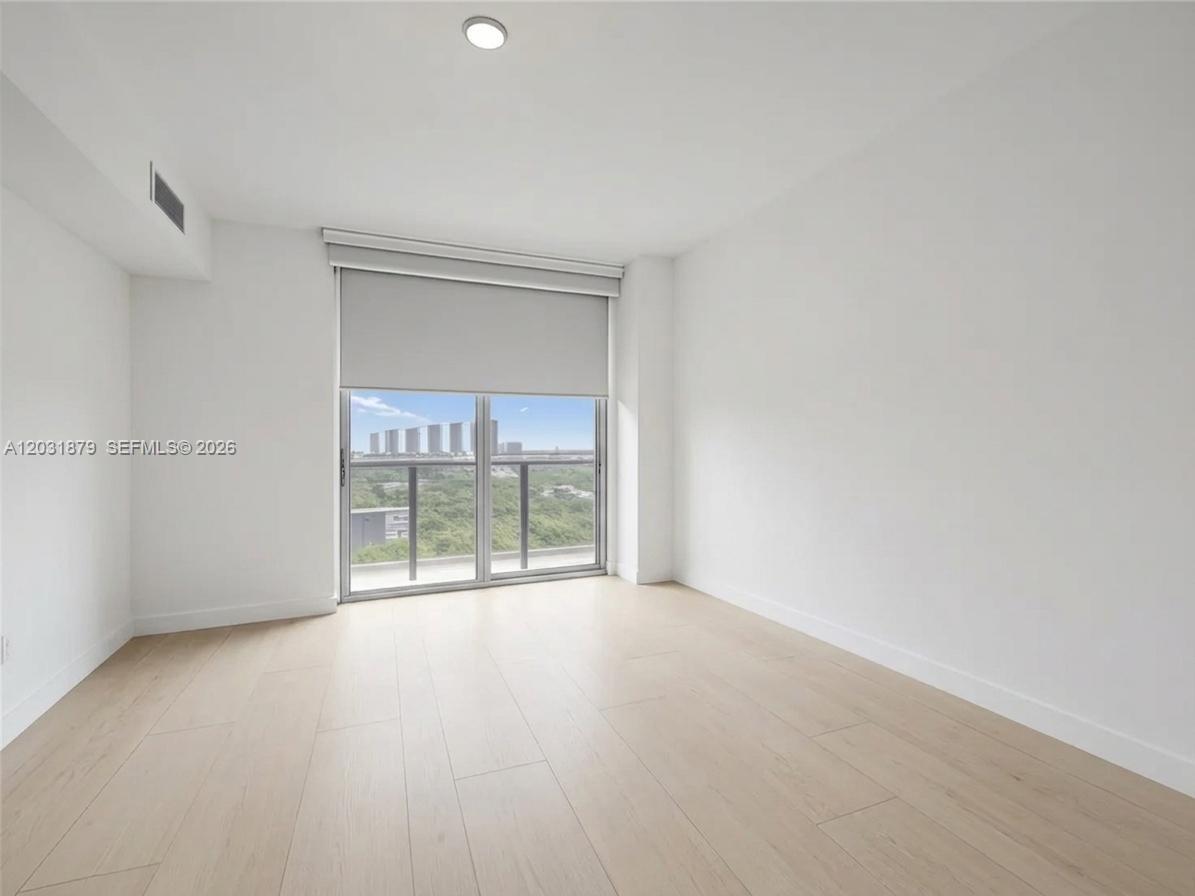An empty room features light wood flooring, white walls, and a sliding glass door — 16385 Biscayne Blvd # 1615, North Miami Beach FL 33160, NORTH MIAMI BEACH, FL