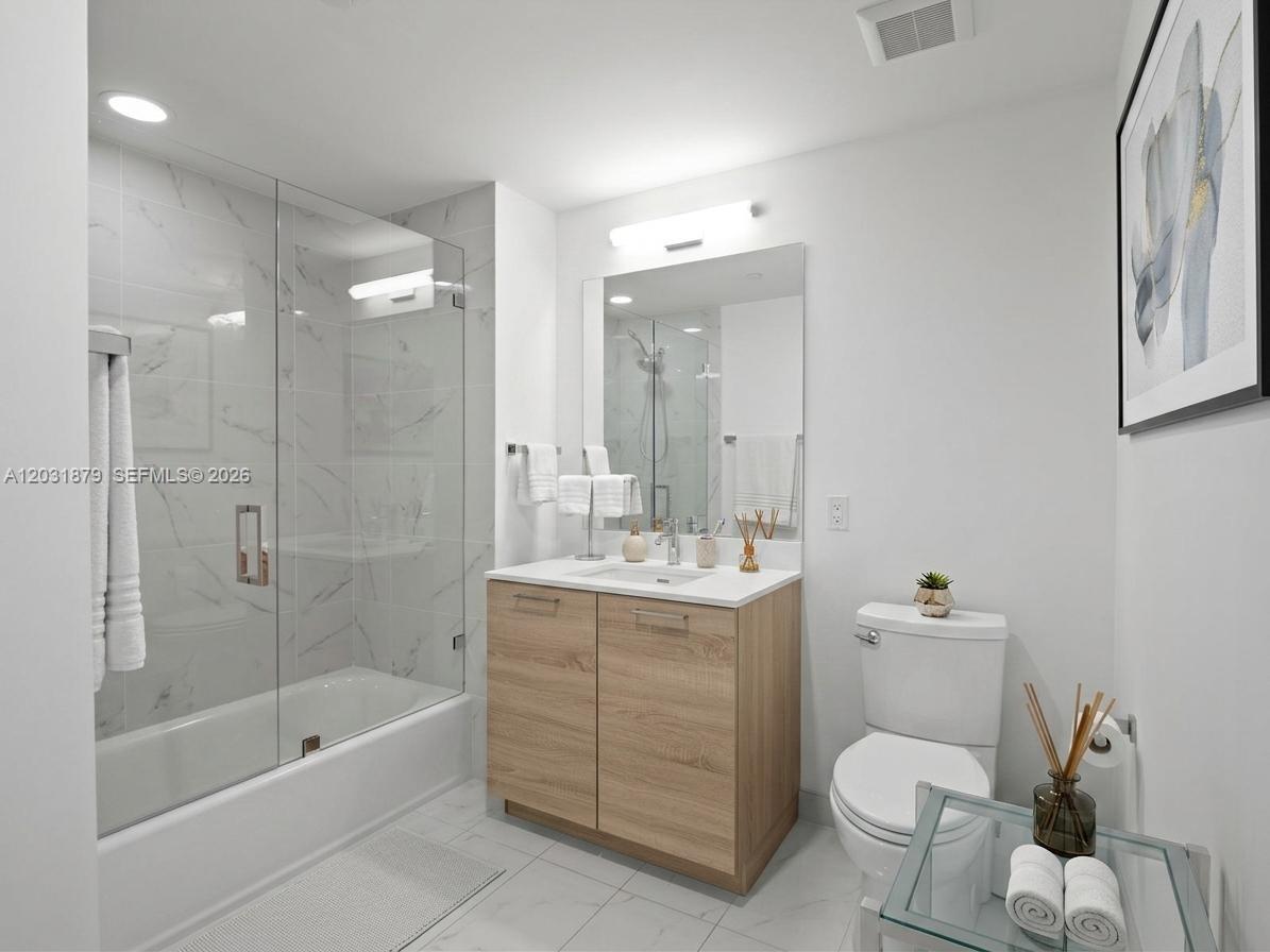 A modern bathroom features a glass-enclosed tub, a wood vanity, and white marble-style tile flooring — 16385 Biscayne Blvd # 1615, North Miami Beach FL 33160, NORTH MIAMI BEACH, FL