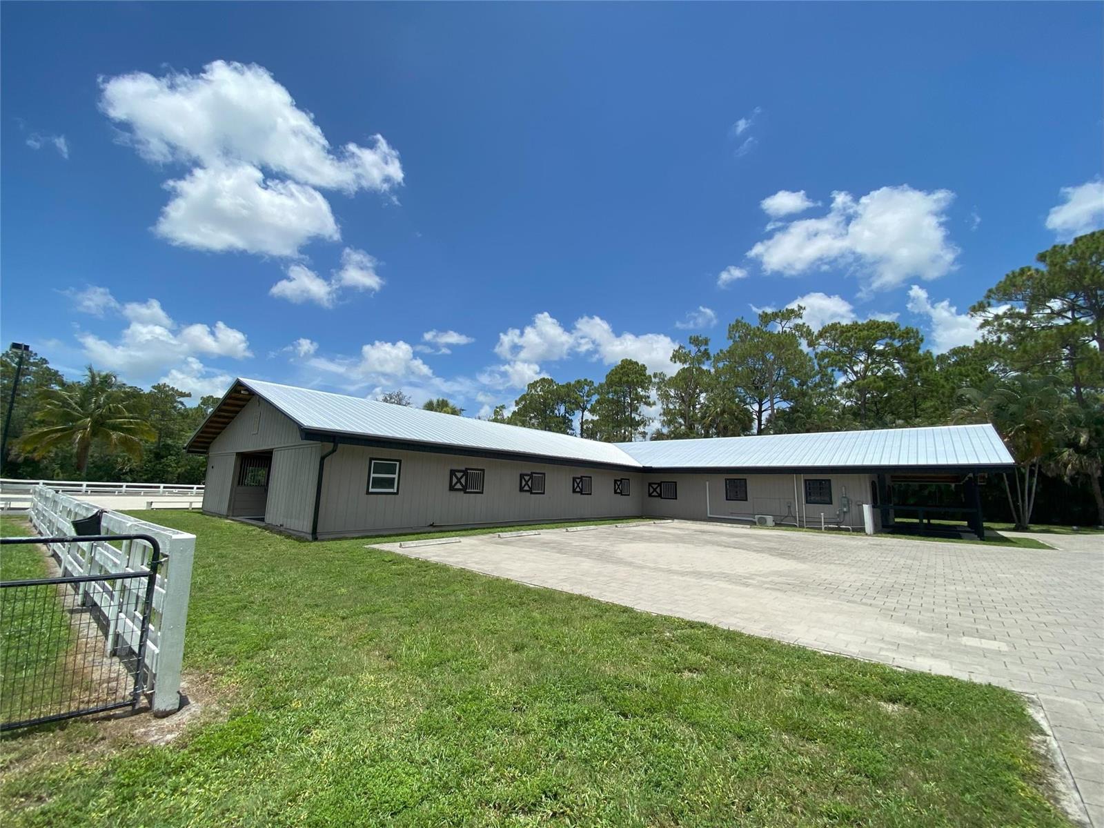 An L-shaped horse stable with a metal roof sits beside a paved parking area — 2315 Deer Run Boulevard, Loxahatchee FL 33470, LOXAHATCHEE, FL