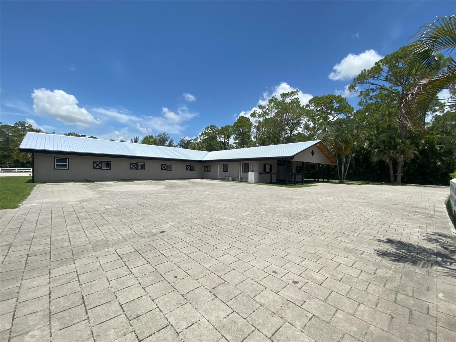 A large, L-shaped horse stable with a metal roof sits beside a paved courtyard — 2315 Deer Run Boulevard, Loxahatchee FL 33470, LOXAHATCHEE, FL