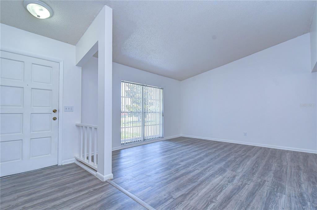 An empty room features light gray wood-look flooring, white walls, and a sliding glass door — 7214 NIA LANE, TAMPA, FL