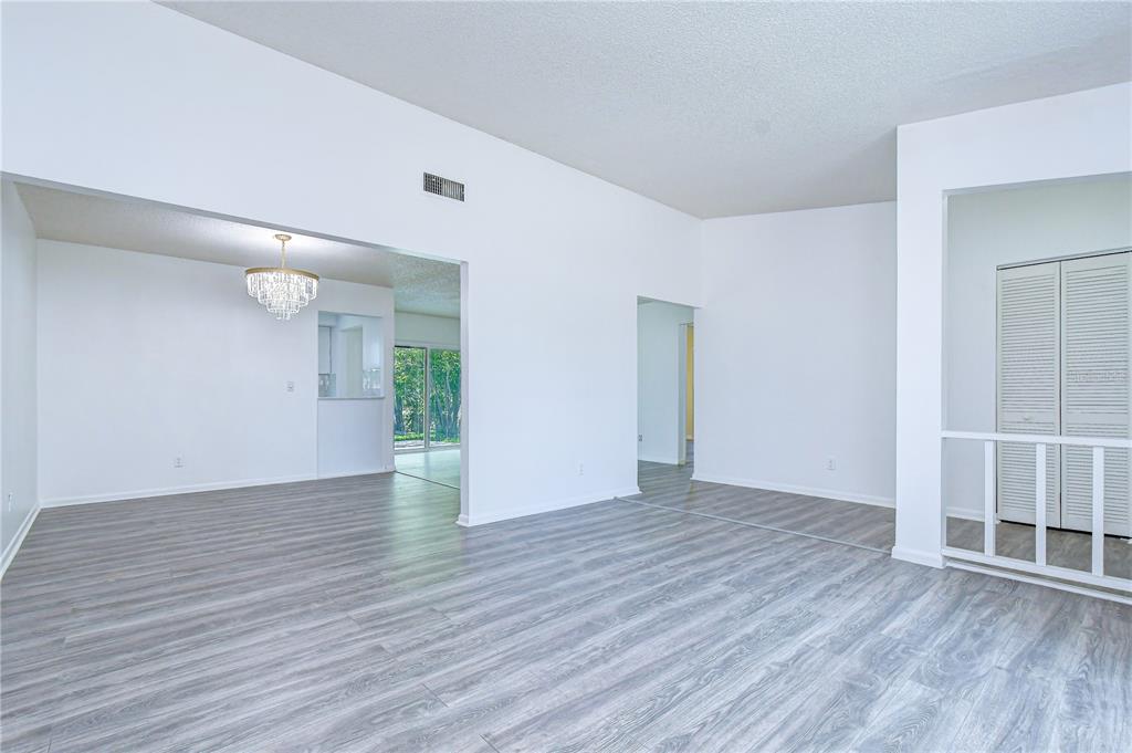 A bright, open-concept living area features light gray wood-look flooring and a white chandelier — 7214 NIA LANE, TAMPA, FL