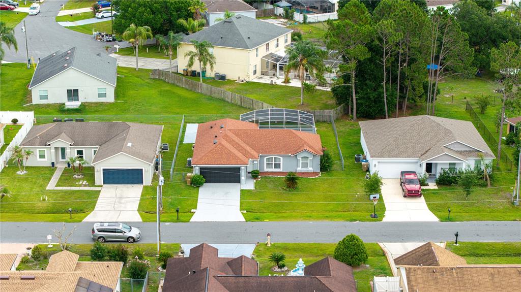 An aerial view shows three suburban houses with driveways and lawns along a paved street — 611 JURA LANE, KISSIMMEE, FL