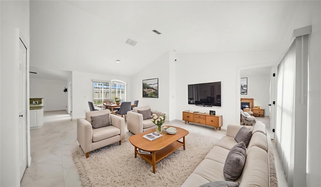 A bright living room features white walls, tile flooring, a vaulted ceiling, and neutral furniture — 611 JURA LANE, KISSIMMEE, FL