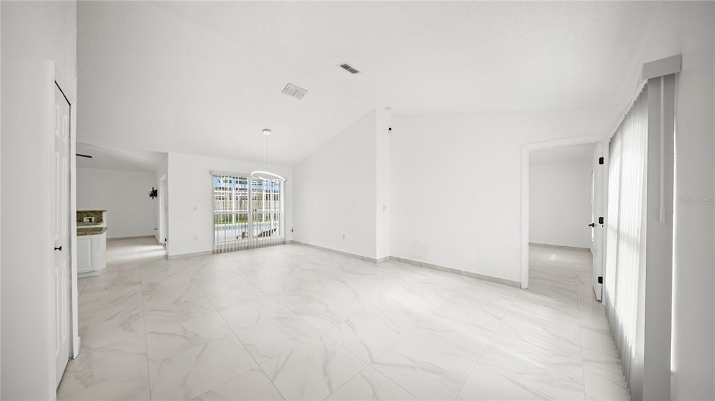 A bright, open-concept living area features white tile flooring, vaulted ceilings, and large windows — 611 JURA LANE, KISSIMMEE, FL