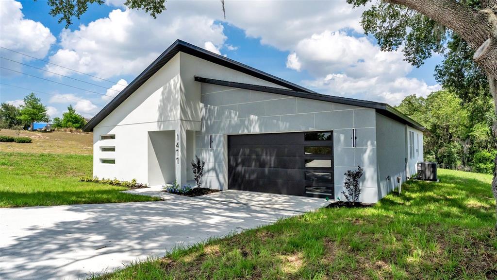 A modern single-story house with a white exterior, gray garage door, and concrete driveway — 1477 HOLLY HILL ROAD, DAVENPORT, FL