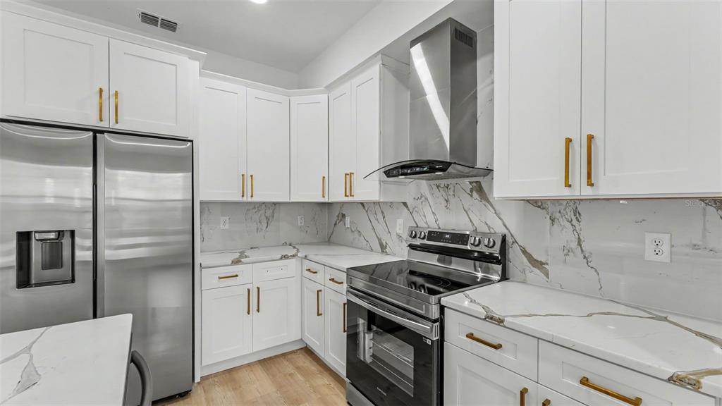 A modern kitchen features white cabinets, gold hardware, stainless steel appliances, and marble-patterned countertops — 1477 HOLLY HILL ROAD, DAVENPORT, FL
