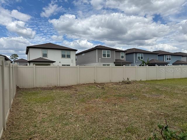 A beige vinyl fence encloses a grassy backyard behind several two-story suburban houses — 30169 SKYLARK DRIVE, WESLEY CHAPEL, FL