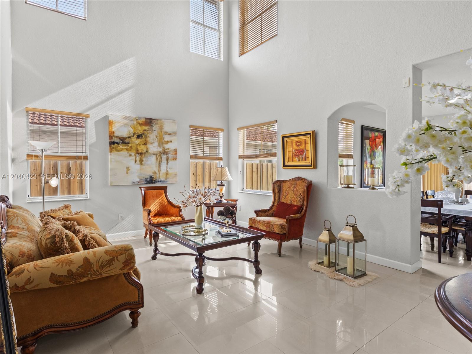 A high-ceilinged living room features tile flooring, traditional furniture, and multiple windows with blinds — 8542 NW 111th Ct, Doral FL 33178, DORAL, FL