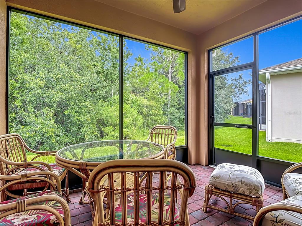 A screened-in patio features wicker furniture, a glass-top table, and views of trees and grass — 700 SHADY CANYON WAY, POINCIANA, FL