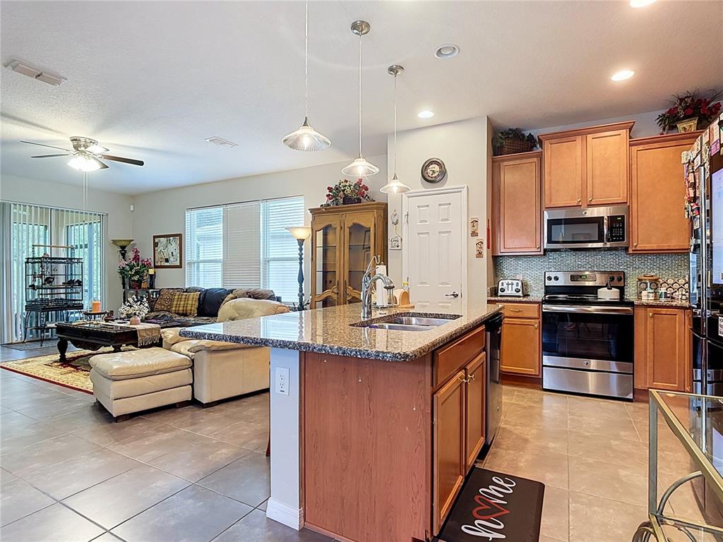 A kitchen with granite countertops and wood cabinets overlooks an open-concept living area — 700 SHADY CANYON WAY, POINCIANA, FL