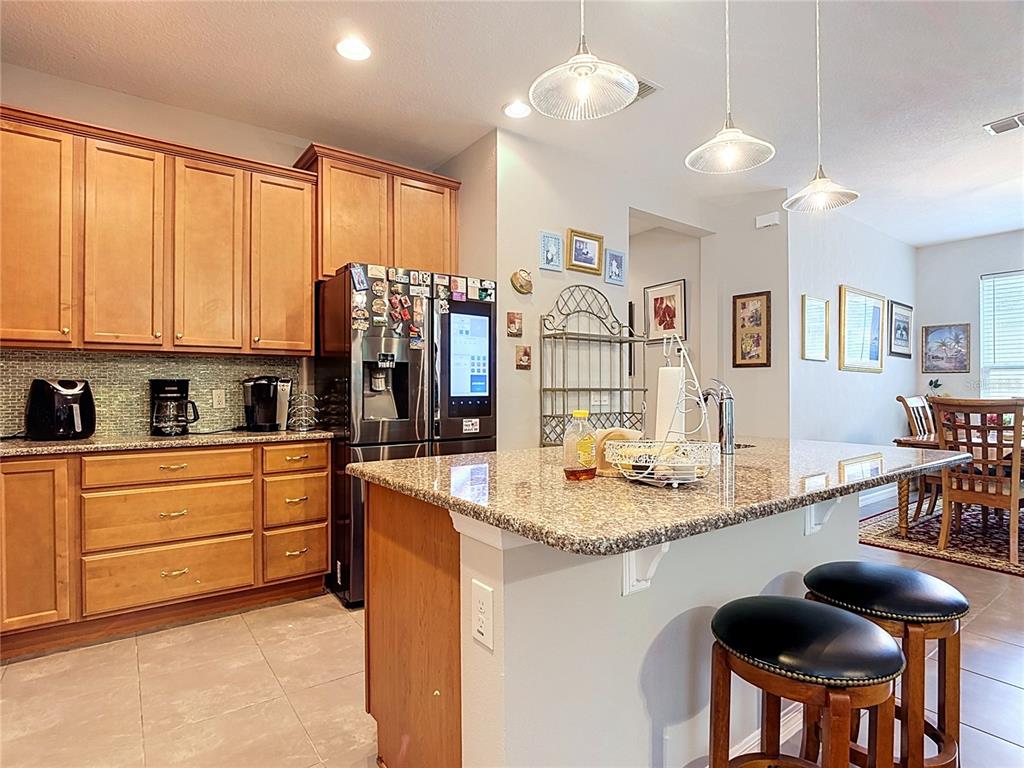 A kitchen features light wood cabinets, granite countertops, a stainless steel refrigerator, and a breakfast island — 700 SHADY CANYON WAY, POINCIANA, FL
