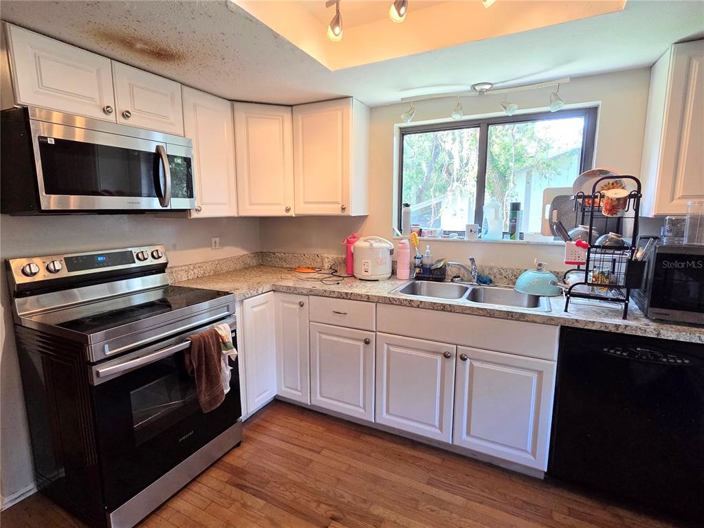 A kitchen with white cabinets, granite countertops, a black dishwasher, and a sliding glass door — 2367 FLANDERS WAY UNIT D, SAFETY HARBOR, FL