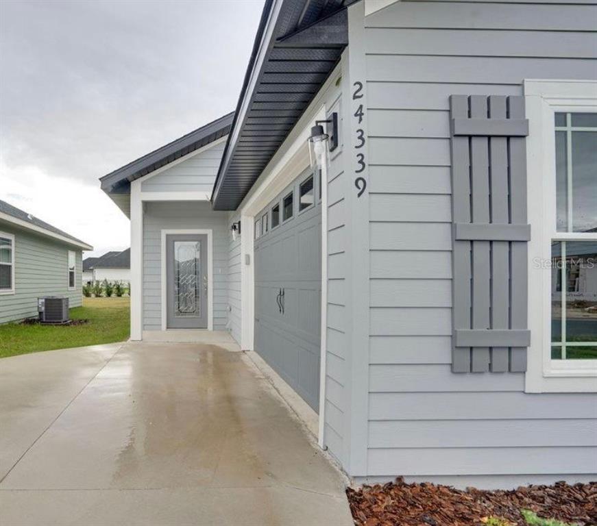 A light gray house exterior features a concrete driveway, a garage, and a side door — 24339 SW 18TH LANE, NEWBERRY, FL