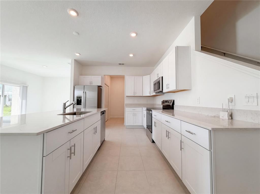 A modern kitchen features white cabinetry, quartz countertops, stainless steel appliances, and tile flooring — 9443 GULF SHORE TERRACE, PARRISH, FL