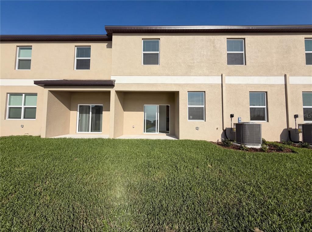 The rear exterior of a two-story townhouse features tan stucco walls, sliding glass doors, and windows — 9443 GULF SHORE TERRACE, PARRISH, FL