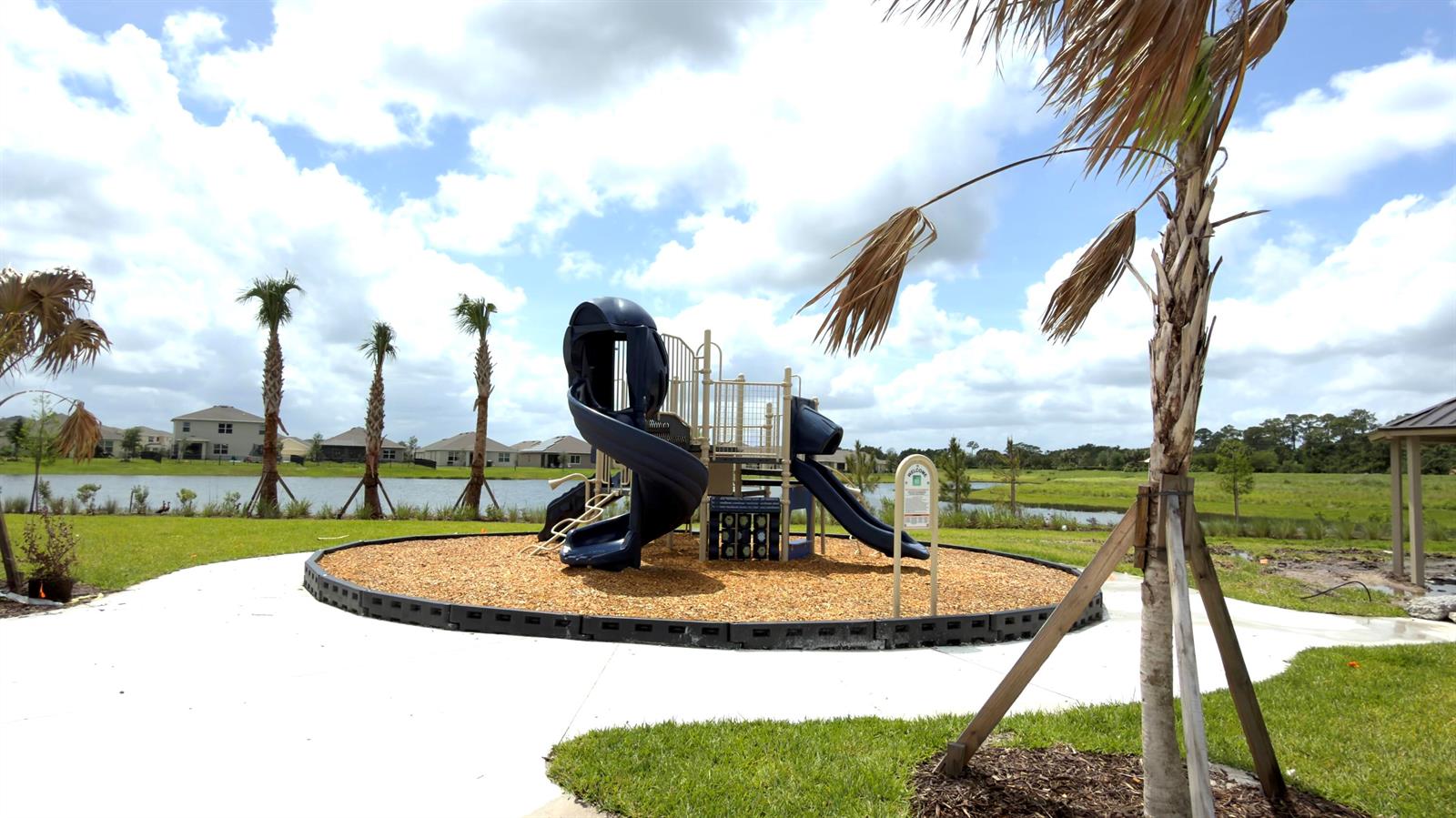 A playground with a blue slide sits on wood chips near a lake and houses — 9617 Potomac Drive, Fort Pierce FL 34945, FORT PIERCE, FL