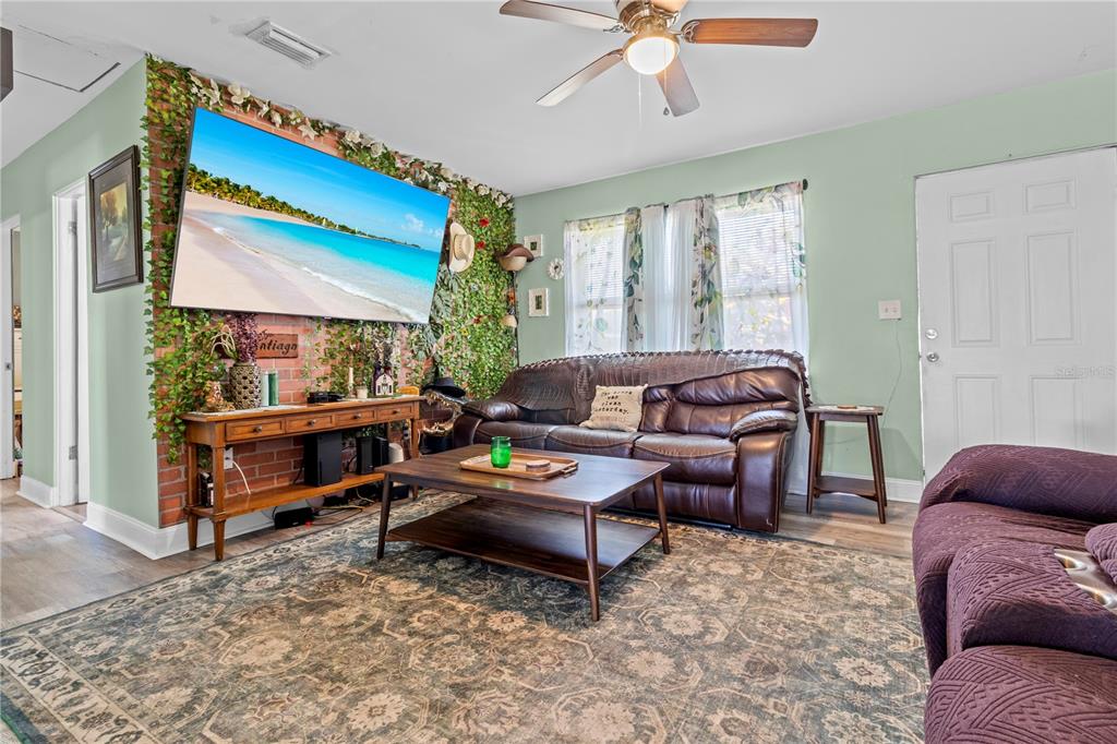 A living room features a brick wall with faux greenery, a television, and leather furniture — 5771 91ST AVENUE N, PINELLAS PARK, FL