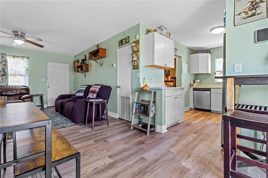 An open-concept living room and kitchen area with light green walls and wood-look flooring — 5771 91ST AVENUE N, PINELLAS PARK, FL