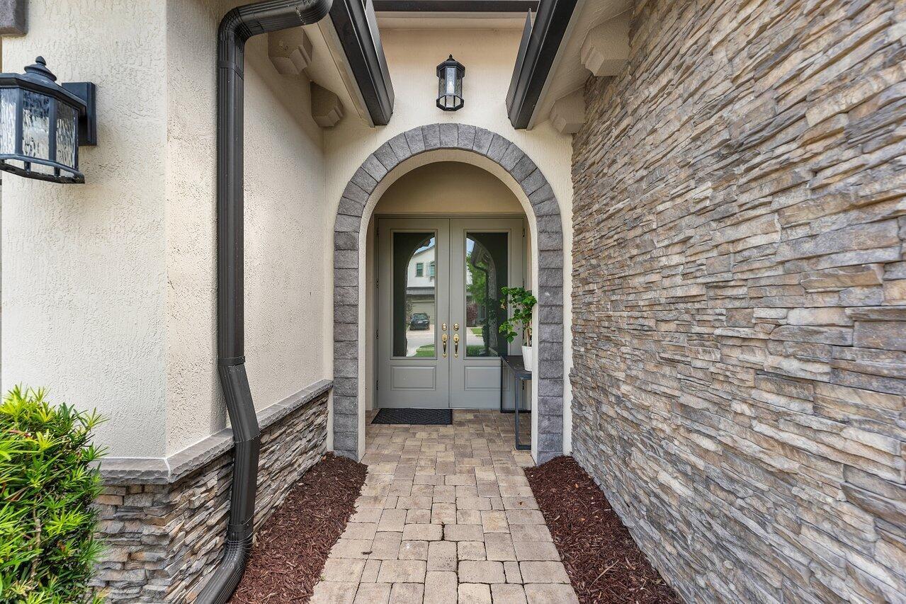 A stone-accented entryway features an arched doorway, double glass doors, and a paved walkway — 9131 Grand Prix Lane, Boynton Beach FL 33472, BOYNTON BEACH, FL
