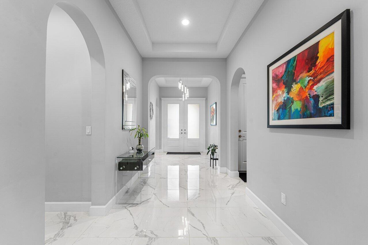 A bright foyer features white marble floors, gray walls, arched doorways, and a colorful abstract painting — 9131 Grand Prix Lane, Boynton Beach FL 33472, BOYNTON BEACH, FL