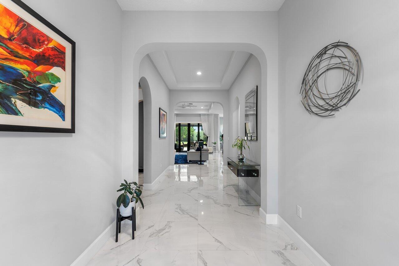 A bright hallway features white marble flooring, arched doorways, and contemporary wall art — 9131 Grand Prix Lane, Boynton Beach FL 33472, BOYNTON BEACH, FL