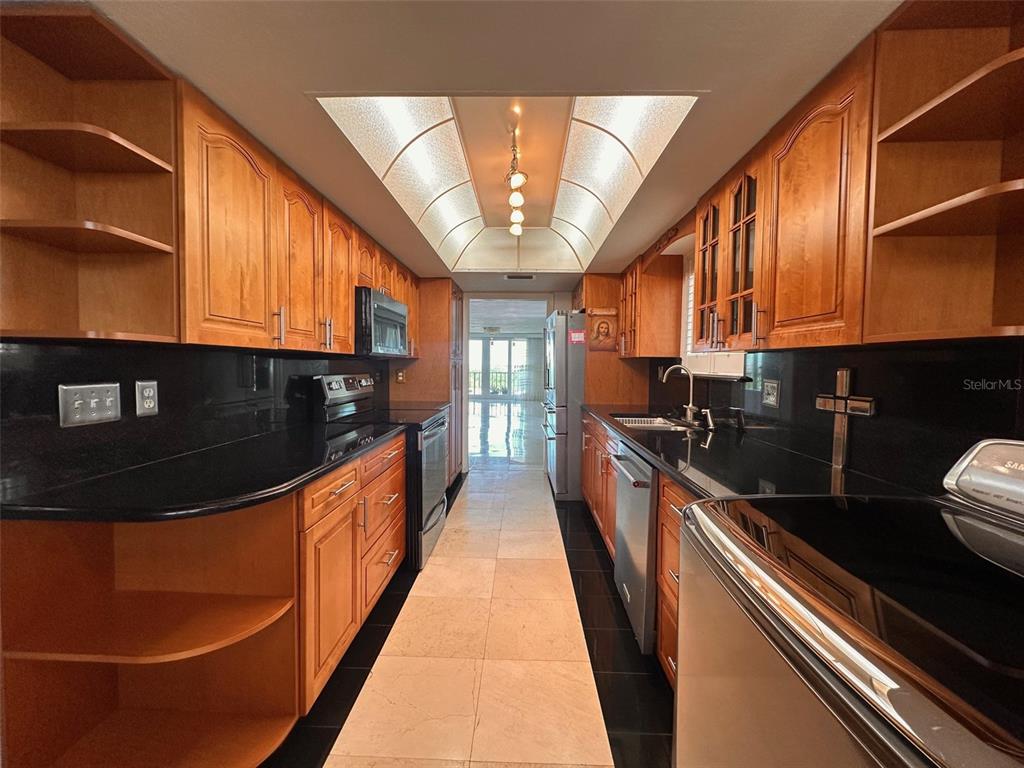 A galley kitchen features wood cabinets, black countertops, stainless steel appliances, and a tray ceiling — 2699 SEVILLE BOULEVARD UNIT 701, CLEARWATER, FL