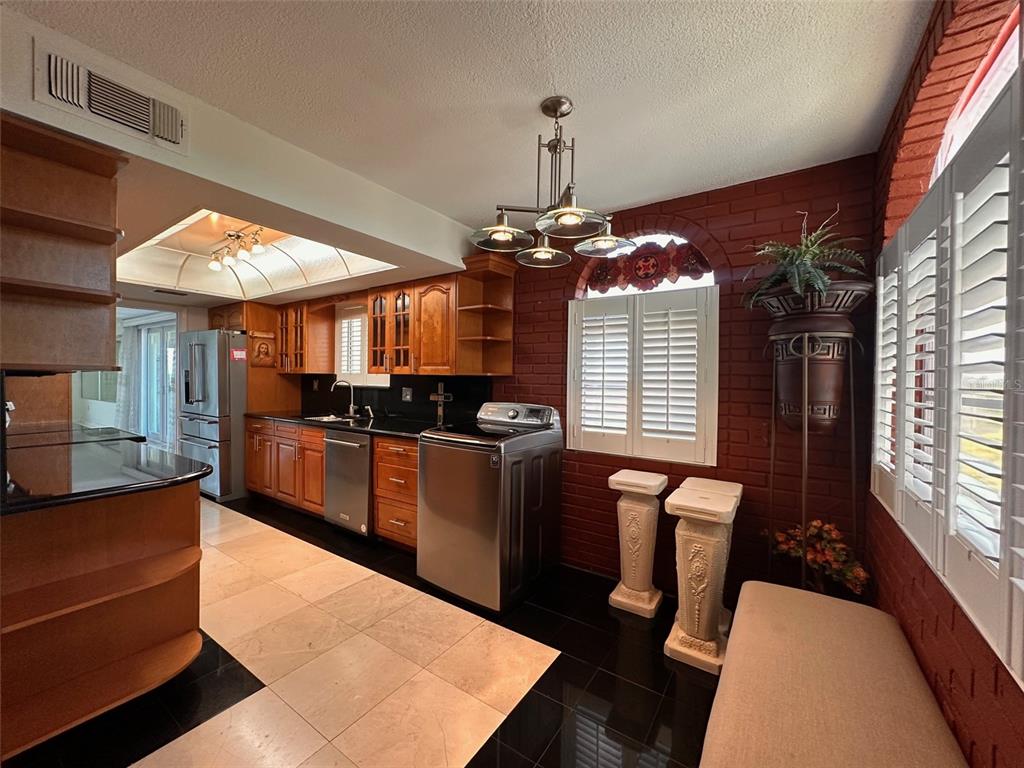 A kitchen with wood cabinets, black countertops, stainless steel appliances, and a red brick wall — 2699 SEVILLE BOULEVARD UNIT 701, CLEARWATER, FL