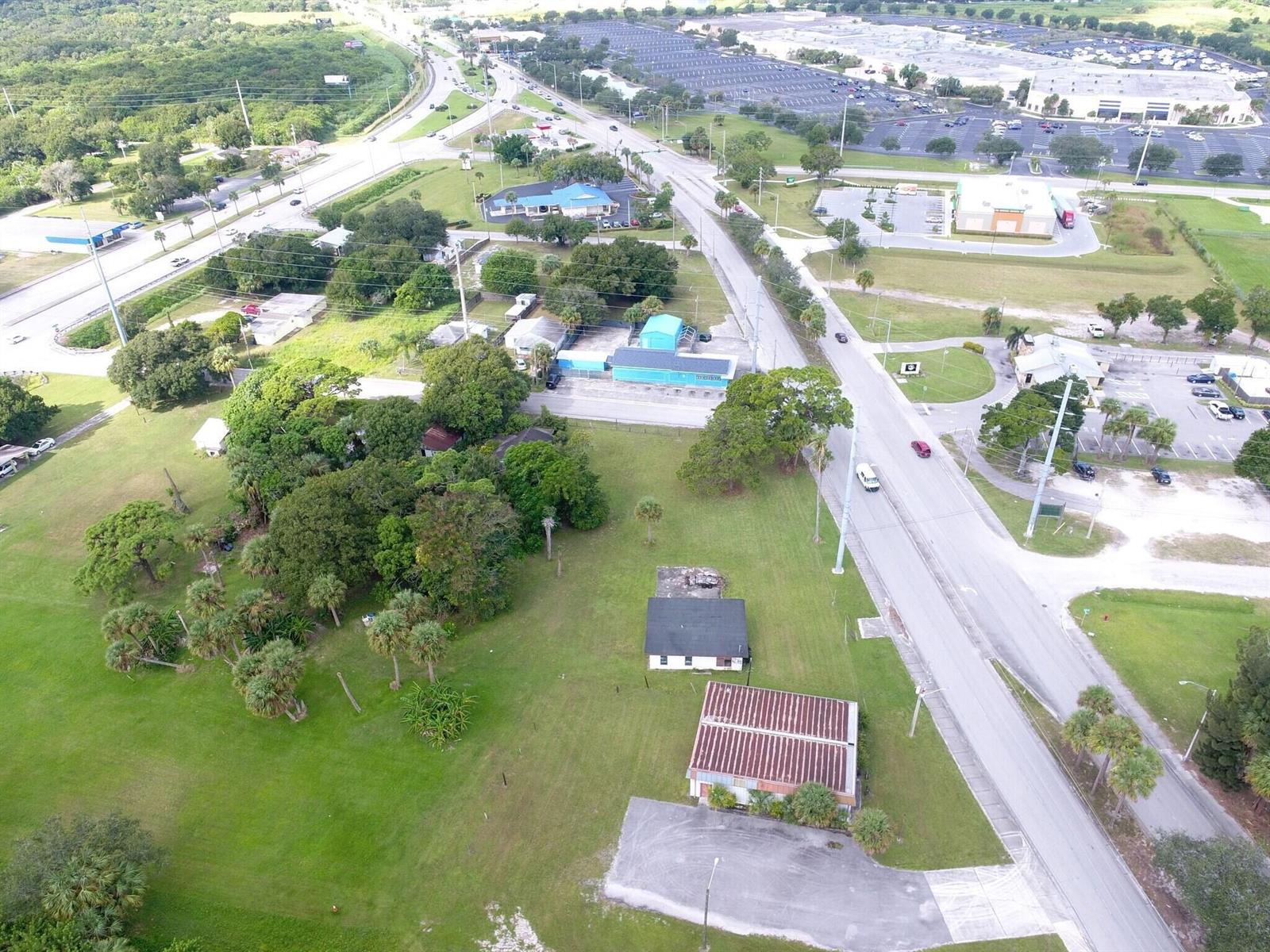 An aerial view shows a grassy lot with two buildings, trees, and adjacent paved roads — 3805 Okeechobee Road, Fort Pierce FL 34947, FORT PIERCE, FL