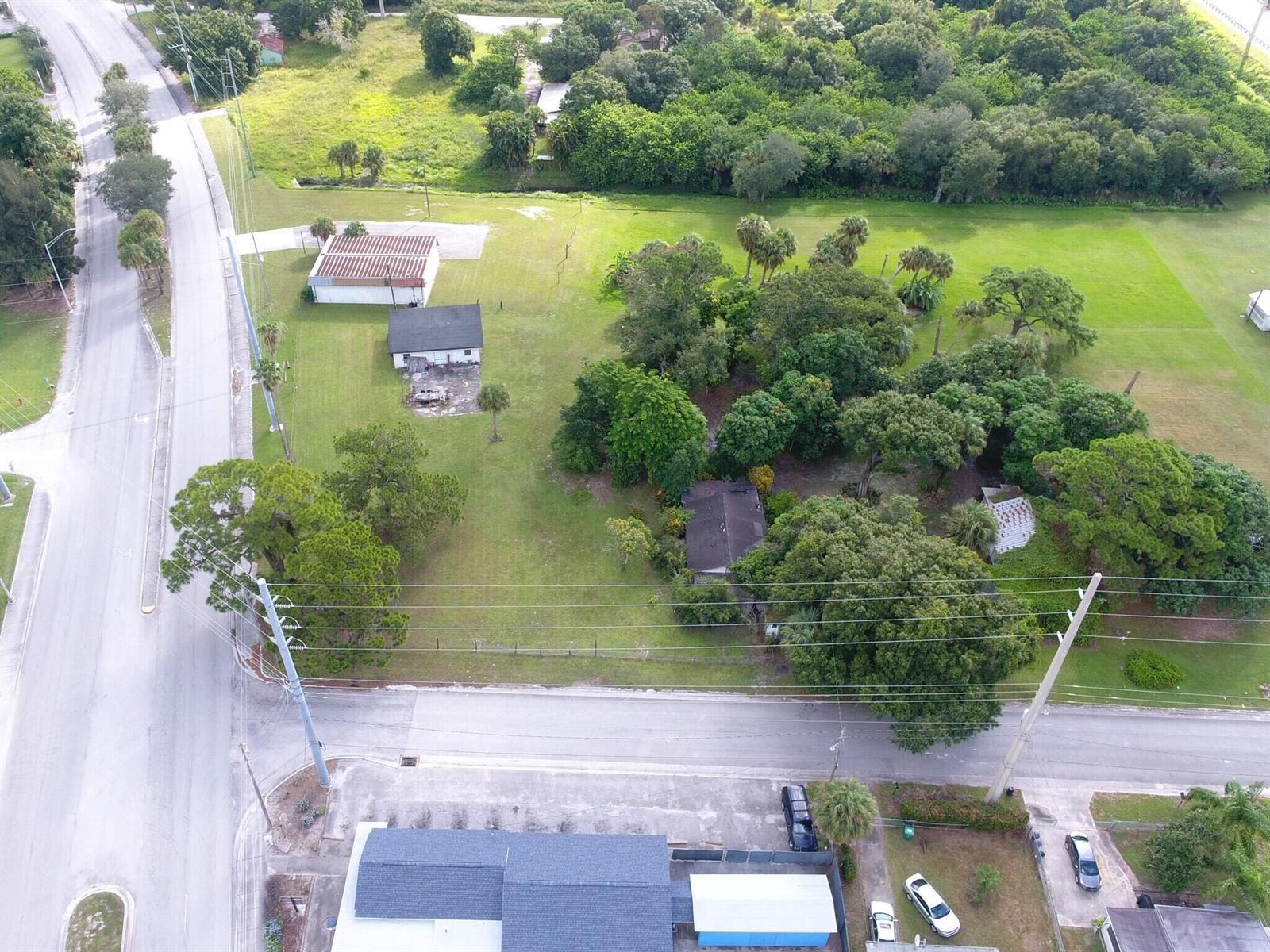 An aerial view shows a large grassy lot with two houses, trees, and nearby roads — 3805 Okeechobee Road, Fort Pierce FL 34947, FORT PIERCE, FL