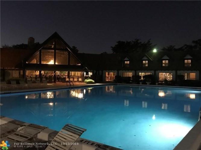A swimming pool sits in front of a building with a large A-frame structure at night — 3670 Inverrary Drive # 3b, Lauderhill FL 33319, LAUDERHILL, FL
