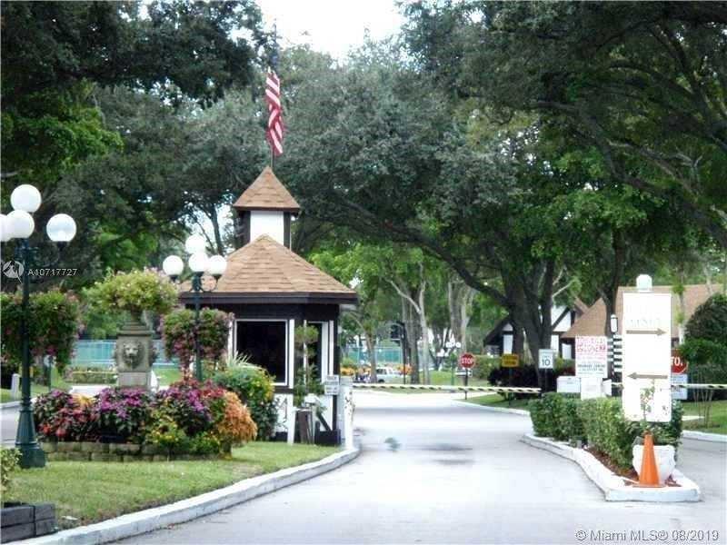A gated entrance features a guardhouse, a flag, and lush landscaping under large trees — 3670 Inverrary Drive # 3b, Lauderhill FL 33319, LAUDERHILL, FL