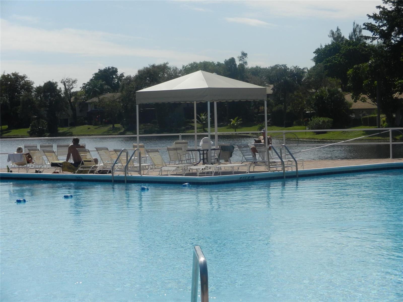 A swimming pool features a covered deck area with lounge chairs overlooking a lake — 3670 Inverrary Drive # 3b, Lauderhill FL 33319, LAUDERHILL, FL