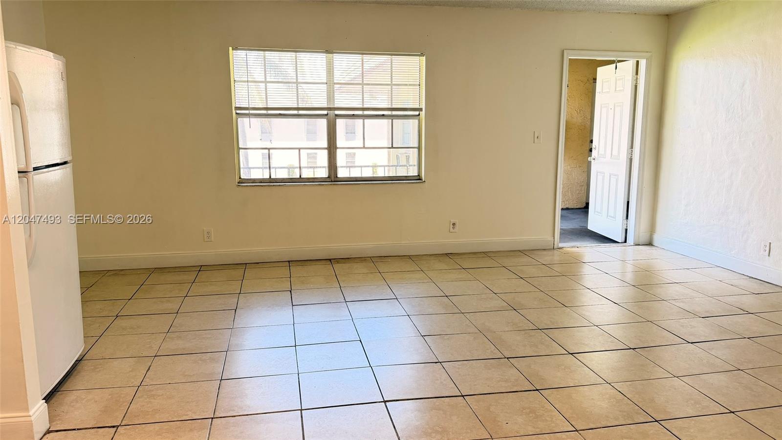 A room with beige tile flooring, a white refrigerator, a window, and an open door — 978 SW 10th Dr # 21, Pompano Beach FL 33060, POMPANO BEACH, FL
