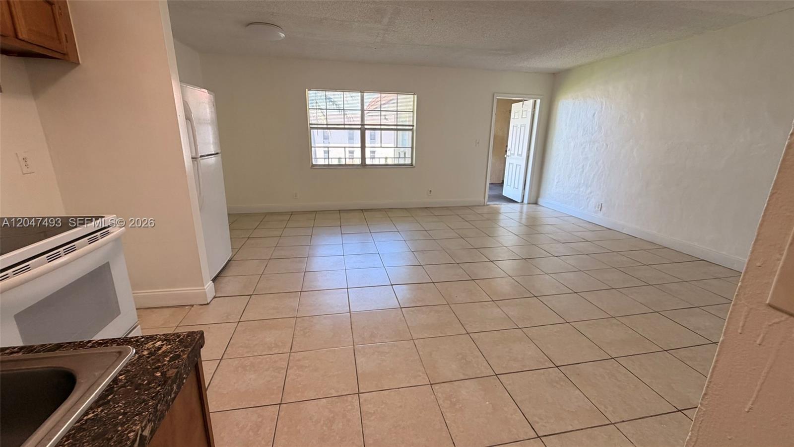 A kitchen area with tile flooring opens into a living room with a window — 978 SW 10th Dr # 21, Pompano Beach FL 33060, POMPANO BEACH, FL