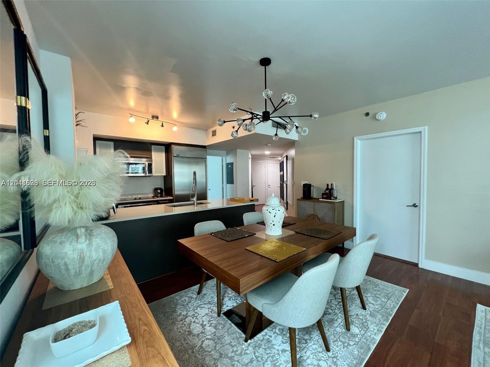 A dining area with a wooden table and modern chandelier sits adjacent to a kitchen — 500 Brickell Ave # 1410, Miami FL 33131, MIAMI, FL