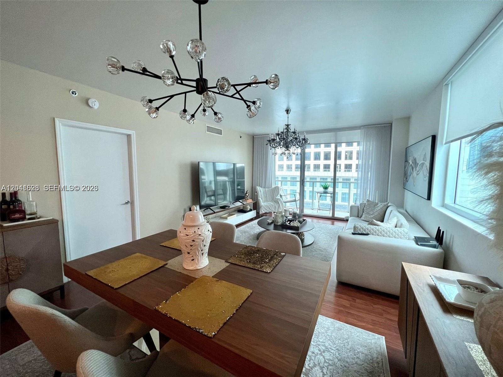 A modern living and dining room features a chandelier, wooden floors, and a balcony view — 500 Brickell Ave # 1410, Miami FL 33131, MIAMI, FL