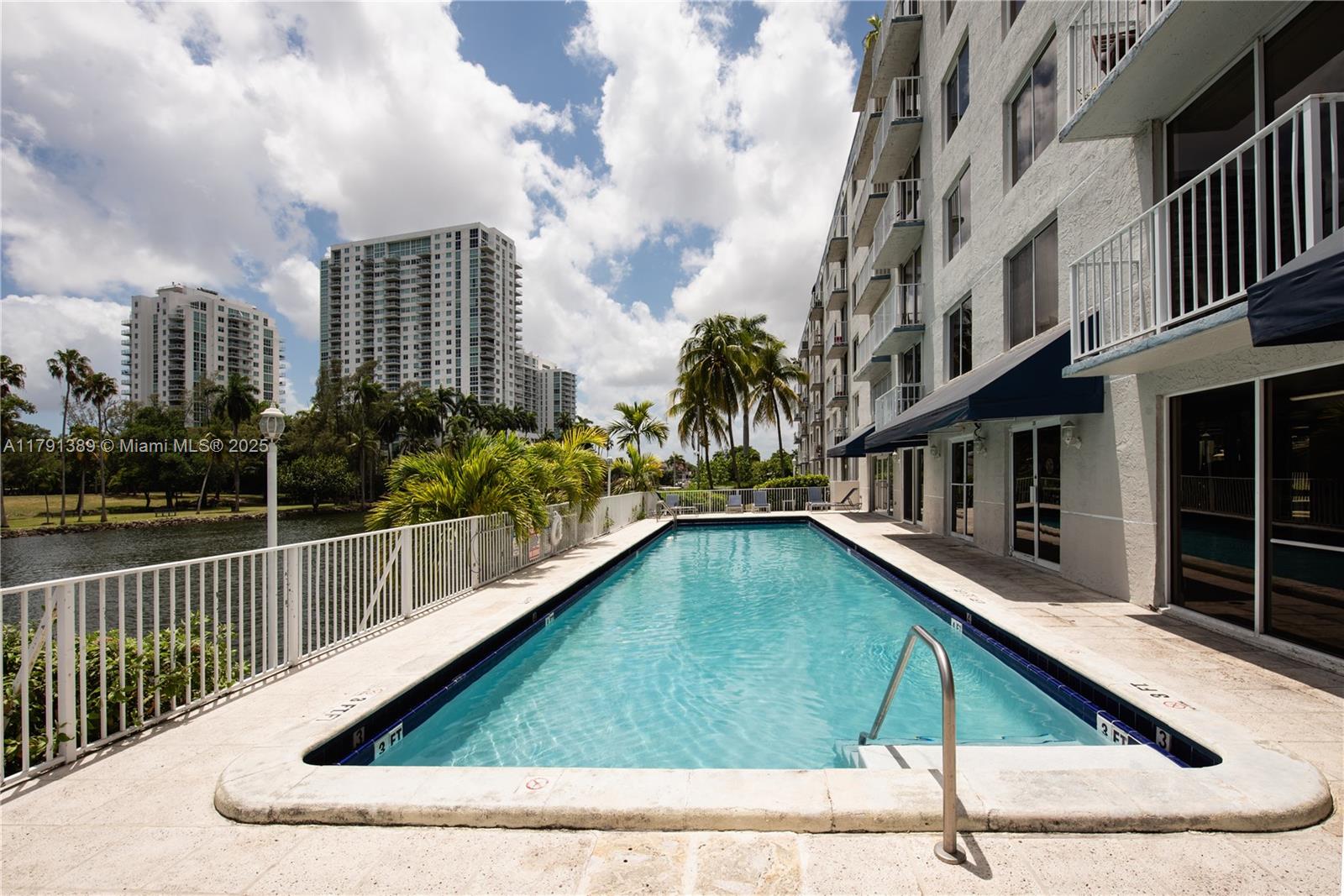 A rectangular swimming pool sits beside a multi-story apartment building with balconies and palm trees — 1720 NW N River Dr # 607, Miami FL 33125, MIAMI, FL