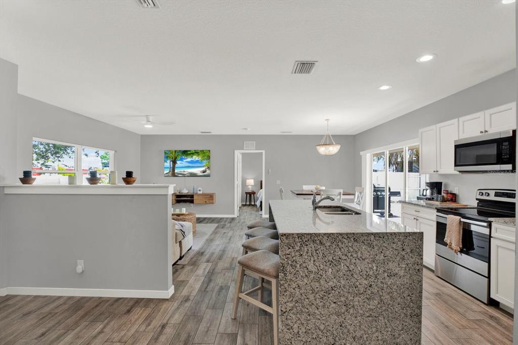 An open-concept kitchen and living area featuring granite countertops, stainless steel appliances, and wood flooring — 2011 OUTER DRIVE, SARASOTA, FL