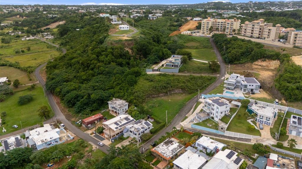 An aerial view shows a residential neighborhood with houses, lush green hills, and paved roads — CARR. 107 INT.BO.BORINQUEN, AGUADILLA, PR