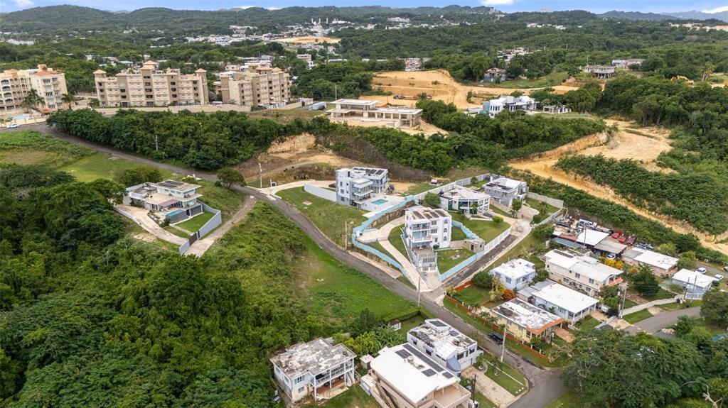 An aerial view shows several modern houses nestled among lush green hills and residential streets — CARR. 107 INT.BO.BORINQUEN, AGUADILLA, PR