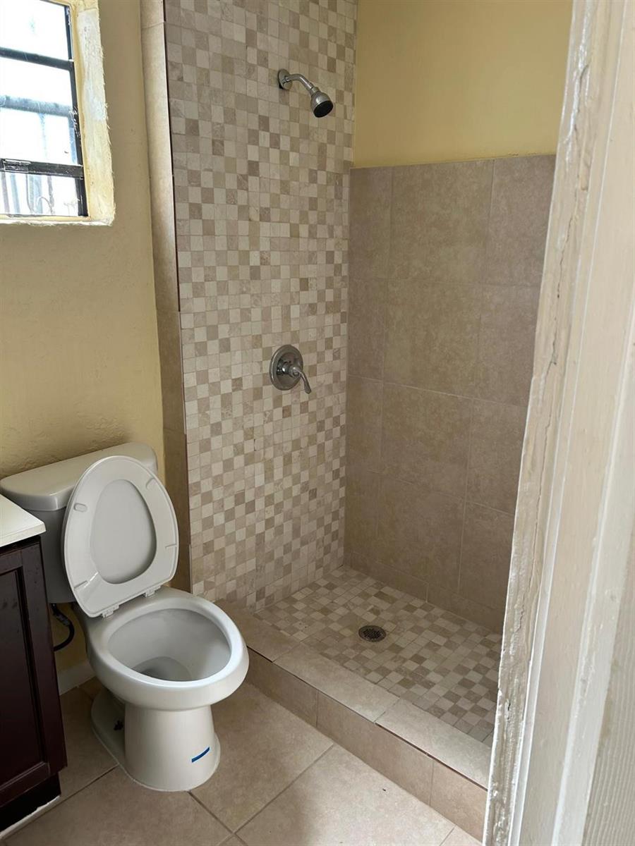 A bathroom features a tiled walk-in shower next to a white toilet — 371 Banyan Avenue, Pahokee FL 33476, PAHOKEE, FL