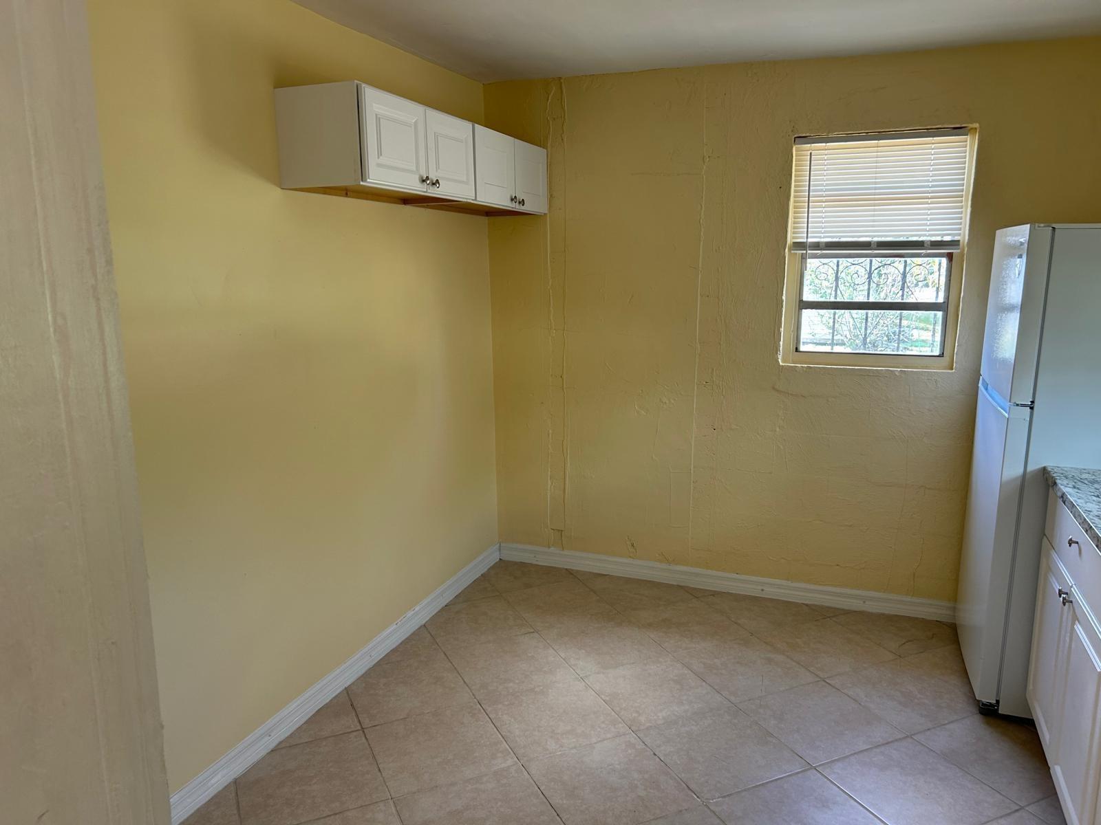 A kitchen corner with yellow walls, tile flooring, white upper cabinets, and a refrigerator — 371 Banyan Avenue, Pahokee FL 33476, PAHOKEE, FL