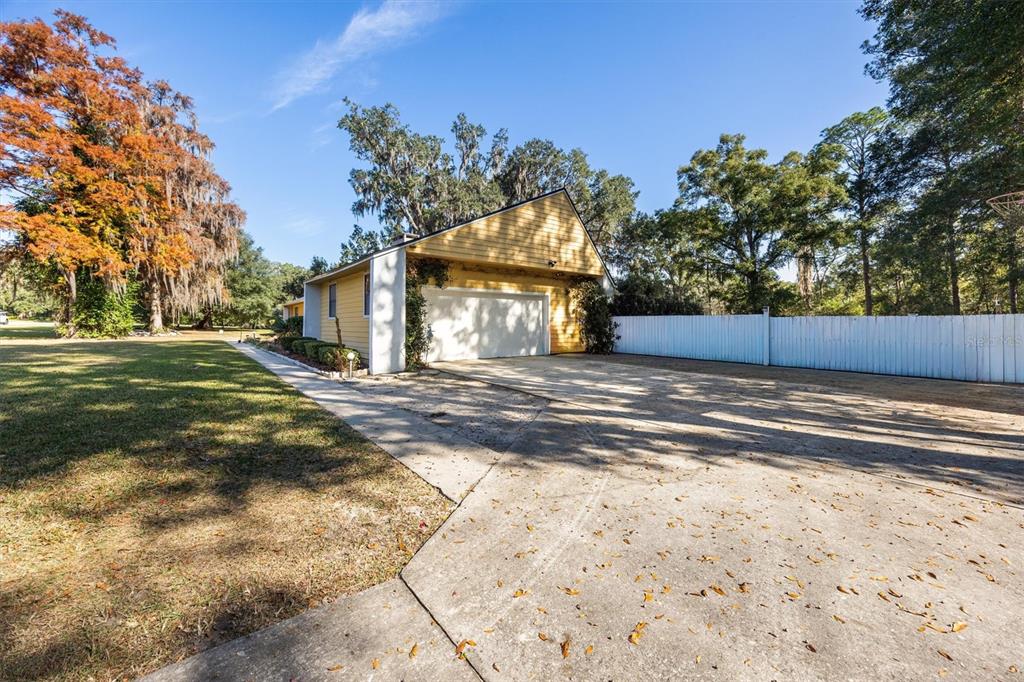 A yellow detached garage sits at the end of a concrete driveway near trees — 3811 SW 82ND STREET, GAINESVILLE, FL
