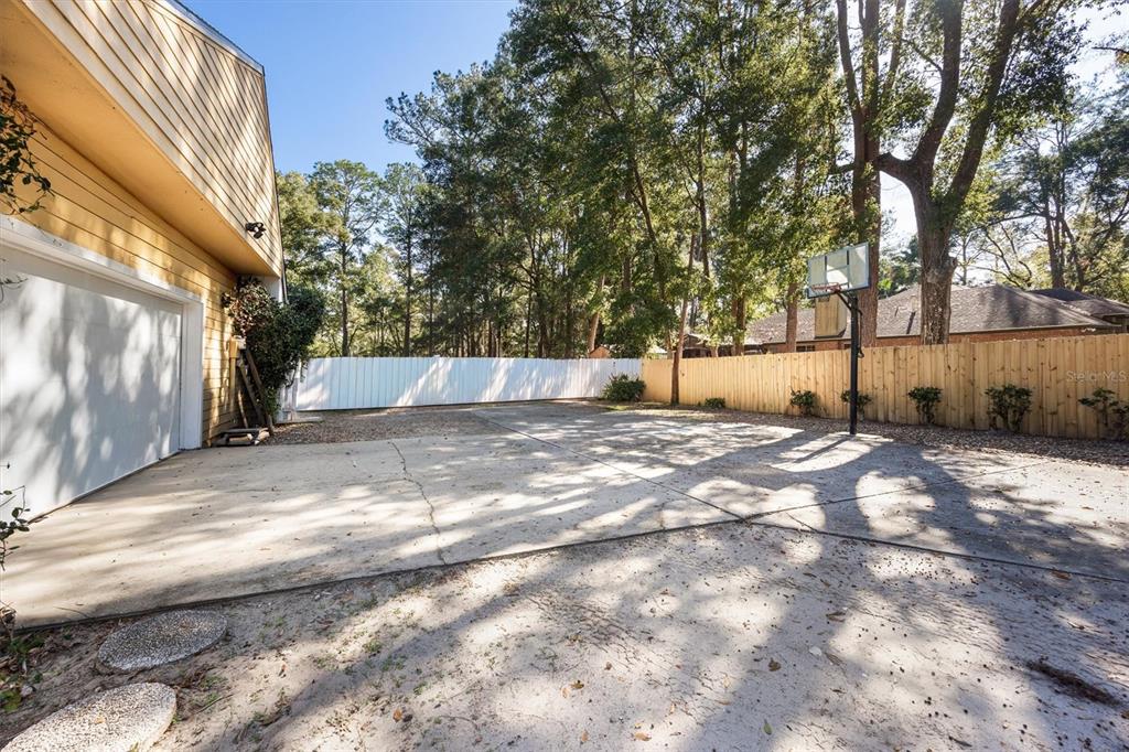 A concrete driveway leads to a garage next to a fenced yard with a basketball hoop — 3811 SW 82ND STREET, GAINESVILLE, FL