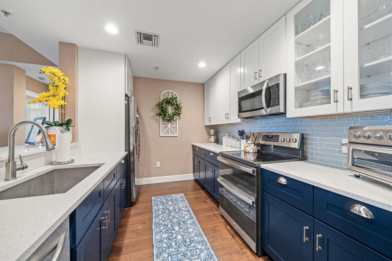 A kitchen features blue lower cabinets, white upper cabinets, a light blue backsplash, and stainless appliances — 1203 Town Center Drive # 313, Jupiter FL 33458, JUPITER, FL